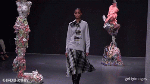 A Model Walks Down The Runway At A Fashion Show Surrounded By Sculptures GIF