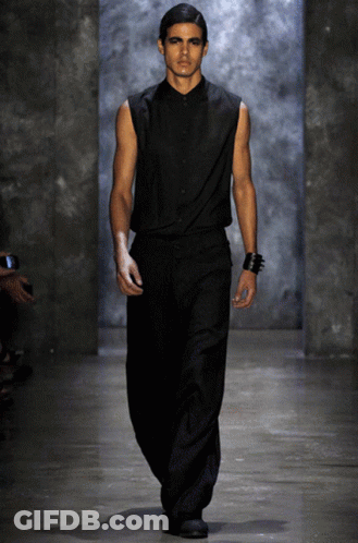 A Model Walks Down The Runway At A Fashion Show Wearing A Black Shirt And Black Pants GIF