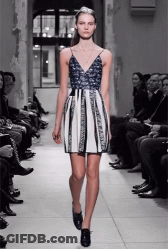 A Model Walks Down The Runway At A Fashion Show Wearing A Blue And White Dress GIF