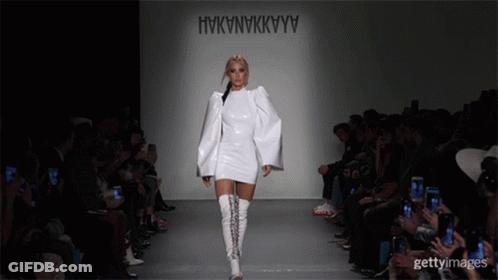 A Model Walks Down The Runway At A Fashion Show Wearing A White Dress And White Boots GIF