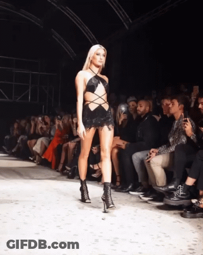 A Model Walks Down The Runway At A Fashion Show While A Crowd Watches GIF