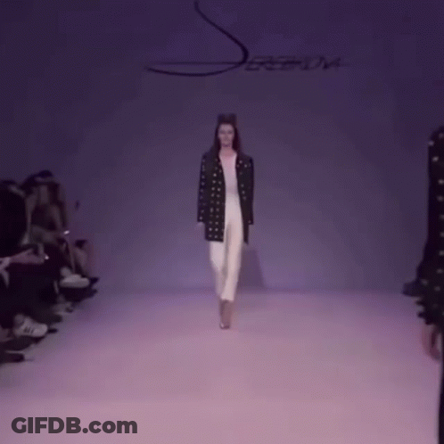 A Model Walks Down The Runway At A Fashion Show With A Purple Background GIF