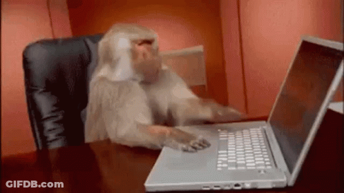 A Monkey Is Sitting At A Desk Using A Laptop GIF
