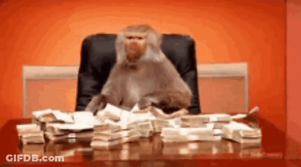 A Monkey Is Sitting At A Desk With Stacks Of Money On It . GIF