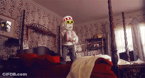 A Monkey Wearing Sunglasses And A Scarf Is Jumping On A Bed In A Bedroom GIF