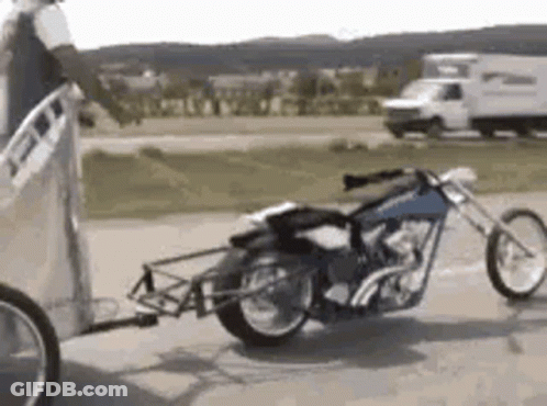 A Motorcycle Is Being Pulled By A Trailer On A Road . GIF