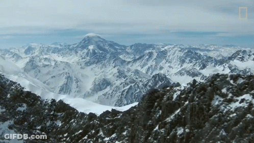 A Mountain Covered In Snow And Rocks With A Mountain In The Background GIF