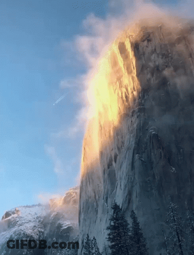 A Mountain Covered In Snow And Trees With The Sun Shining On It GIF