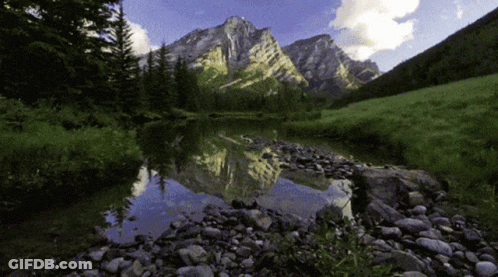 A Mountain Is Reflected In A Lake With Rocks In The Foreground GIF