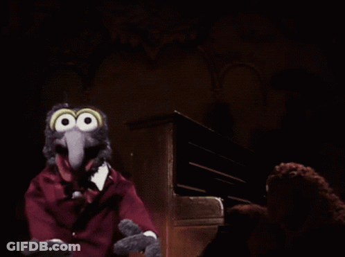 A Muppet With Big Eyes And A Red Suit Is Sitting In Front Of A Piano GIF