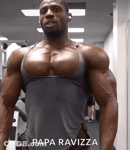 A Muscular Man In A Grey Tank Top Is Standing In A Gym With Papa Ravizza Written On The Bottom Of His Chest . GIF