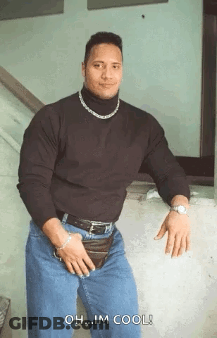 A Muscular Man Wearing A Black Turtleneck And Jeans Is Standing In Front Of A Wall . GIF