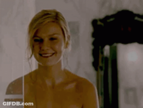 A Naked Woman Is Smiling In Front Of A Mirror In A Dark Room . GIF