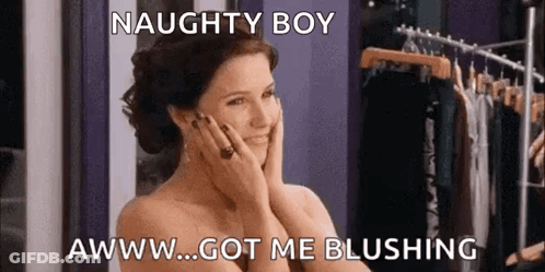 A Naked Woman Is Standing In Front Of A Clothes Rack With Her Hands On Her Face And Smiling . GIF