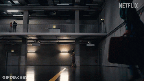 A Netflix Ad Shows A Woman Carrying A Briefcase Walking In A Dark Room GIF