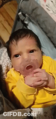 A Newborn Baby Is Holding A Pacifier In His Mouth . GIF