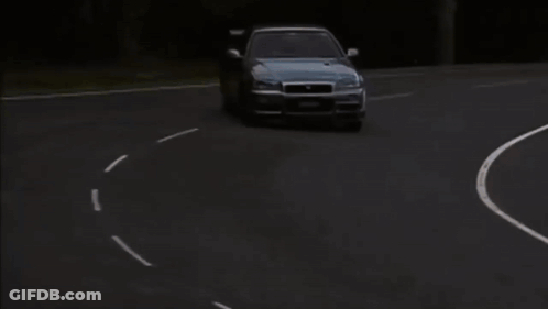 A Nissan Car Is Driving Down A Road With A Grassy Hill In The Background GIF