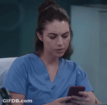 A Nurse In A Blue Scrub Top Is Looking At Her Cell Phone . GIF