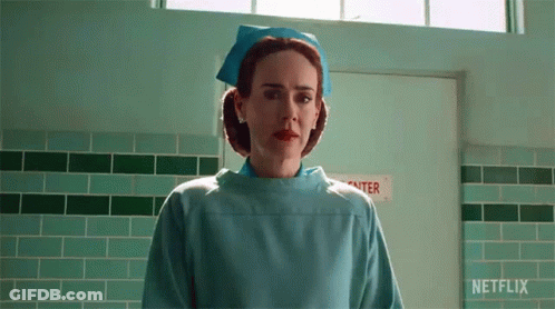 A Nurse In A Blue Uniform Is Standing In A Hallway . GIF