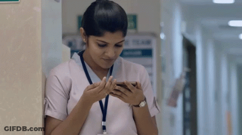 A Nurse Is Leaning Against A Wall And Looking At Her Phone GIF