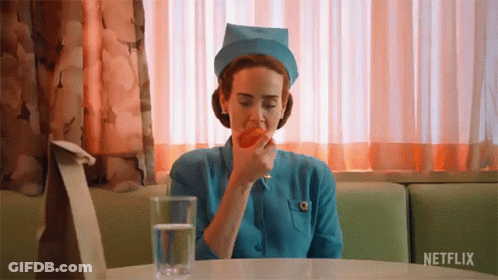 A Nurse Is Sitting At A Table With A Glass Of Water And An Apple In Her Mouth . GIF