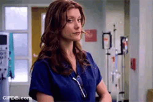 A Nurse Is Standing In A Hospital Room Wearing A Blue Scrub Top . GIF