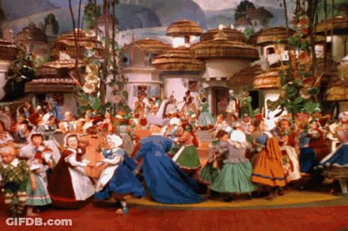 A Painting Of A Group Of People Dancing In Front Of A Village With Thatched Roofs GIF