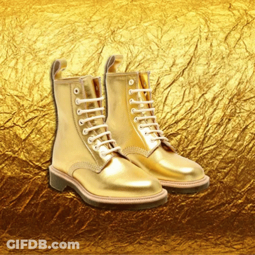 A Pair Of Gold Boots With White Laces Are Against A Gold Background GIF