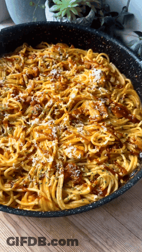 A Pan Filled With Noodles And Sauce On A Wooden Table GIF