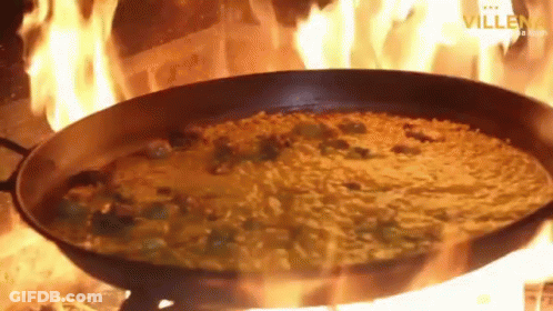 A Pan Of Food Is Being Cooked On A Stove With Flames Coming Out Of It .. GIF