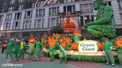 A Parade With A Green Giant Float In The Middle GIF