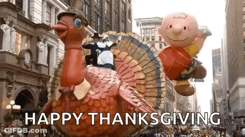 A Parade With A Turkey Float And Charlie Brown Balloons Flying In The Air . GIF