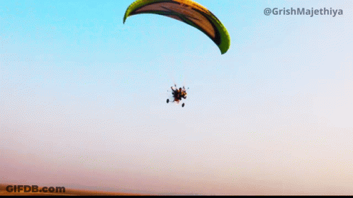 A Paraglider Is Flying Through A Blue Sky With The Hashtag @Grishmajethiya On The Bottom GIF