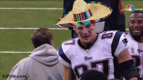 A Patriots Player Wearing A Sombrero Is Talking To A Man GIF