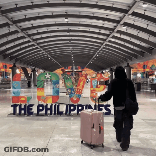 A Person Carrying A Suitcase Walking In Front Of A Sign That Says The Philippines GIF