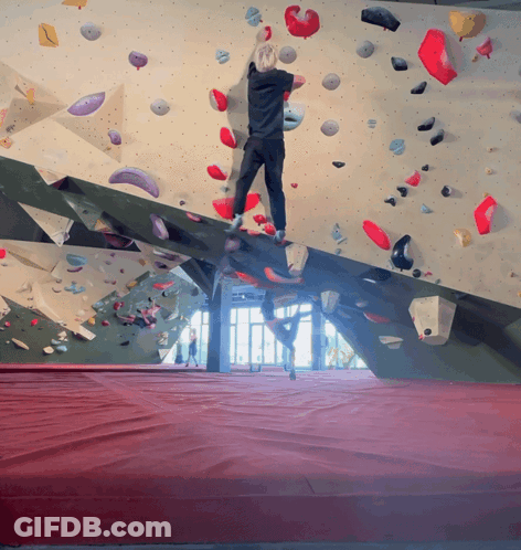 A Person Climbs A Climbing Wall With A Red Mat GIF