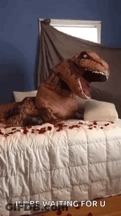A Person Dressed As A T-Rex Is Sitting On A Bed . GIF