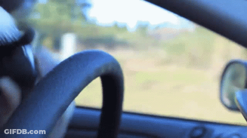 A Person Driving A Car With A Steering Wheel In The Foreground And A Rear View Mirror In The Background GIF