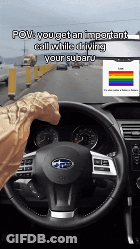 A Person Driving A Subaru With A Rainbow Flag On The Dashboard GIF