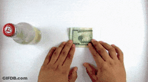 A Person Folding A Dollar Bill Next To A Bottle With A Red Cap GIF