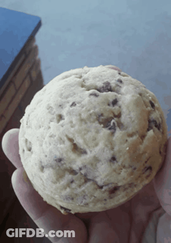 A Person Holding A Cookie In Their Hand With Chocolate Chips On It GIF