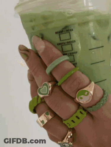 A Person Holding A Cup Of Green Tea With A Lot Of Rings On Their Hands GIF