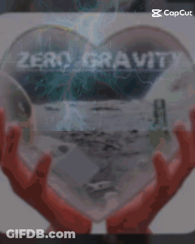 A Person Holding A Heart Shaped Object With The Word Zero Gravity On It GIF
