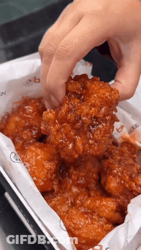 A Person Holding A Piece Of Fried Chicken Over A Box Of Chicken GIF