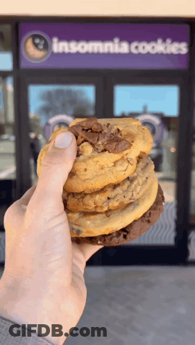 A Person Holding A Stack Of Cookies In Front Of An Insomnia Cookies Store GIF