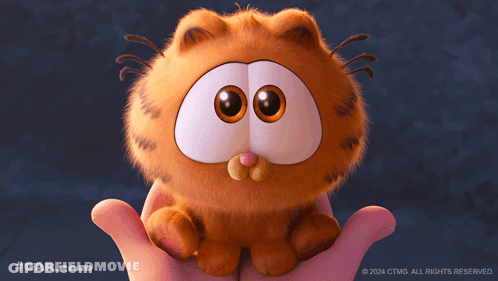 A Person Holding A Stuffed Garfield Cat With A Nut In Its Mouth GIF