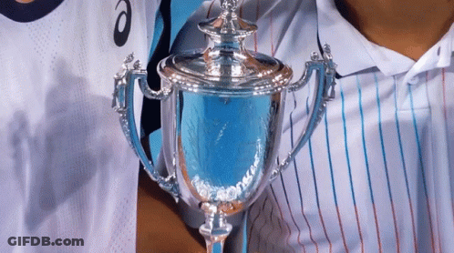 A Person Holding A Trophy In Front Of A Person Wearing A Shirt That Says Asics GIF