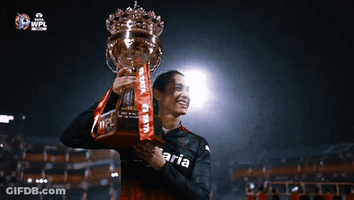 A Person Holding A Trophy With The Word Aria On Their Shirt GIF