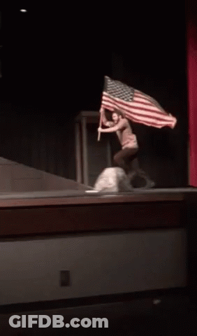 A Person Holding An American Flag On A Stage In A Dark Room GIF