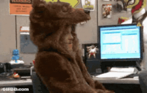 A Person In A Bear Costume Is Sitting At A Desk In Front Of A Computer GIF